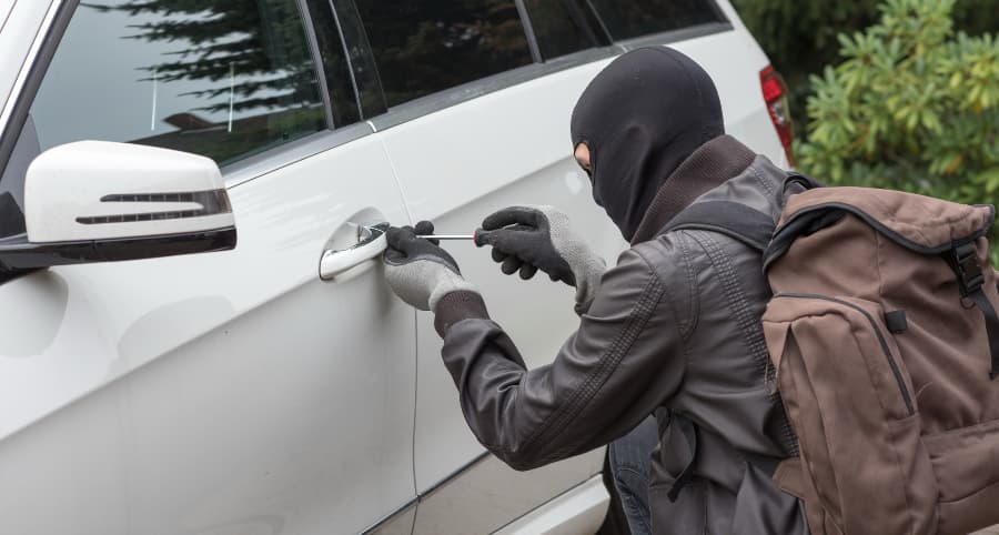 Thief breaking into a white vehicle in a residential setting